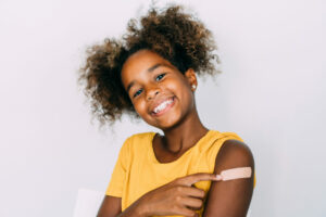 Girl smiling and pointing at arm where she received vaccination